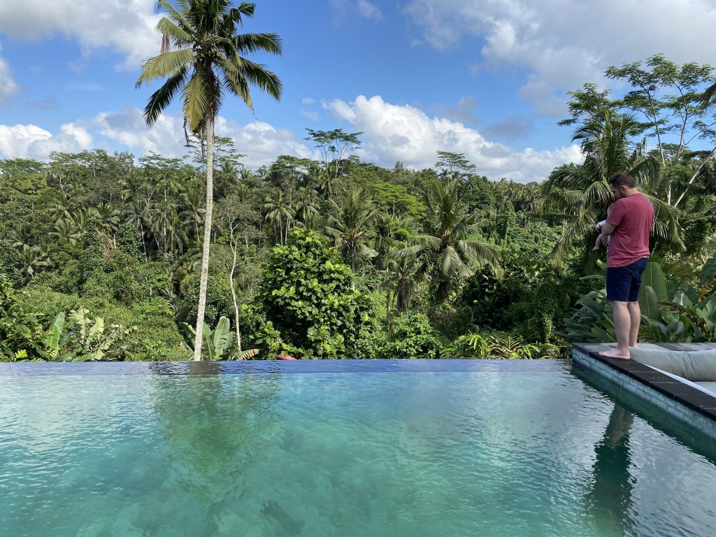 Vater hält Baby am Rand eines Infinity Pools mit Blick auf den Dschungel von Bali
