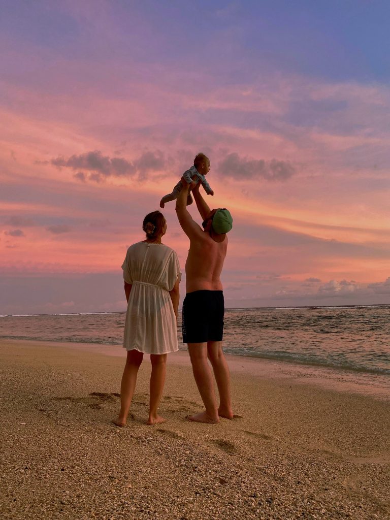 Familie am Strand bei magischem Sonnenuntergang auf Bali - Elternzeitreise mit 5 Monate altem Baby